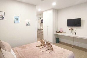 A bedroom with a bed, a TV, and a kitchenette in the background. - Classy at Bangsaen @The East Ville Bangsaen (Chon Buri)