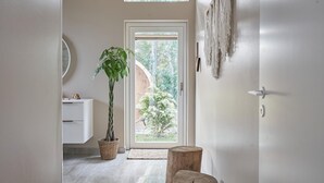 A hallway with a white door leading to a balcony, a potted plant, a round mirror, and a wooden stool.