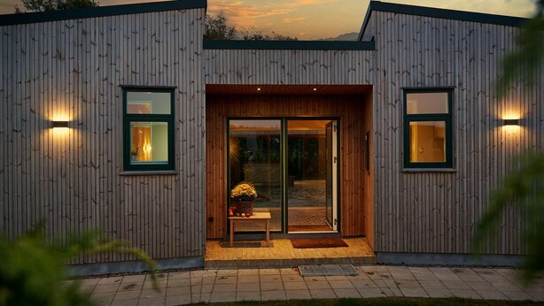 A modern building with a wooden exterior, a glass door entrance, and a small outdoor seating area with a table and chairs.