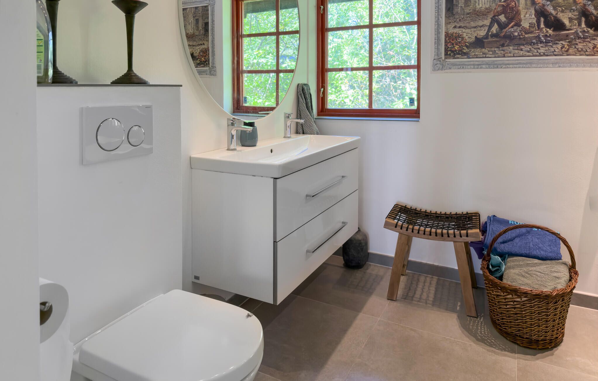 Ein Badezimmer mit Toilette, Waschbecken mit Spiegel, einem Fenster und einem Korbwannenstuhl.