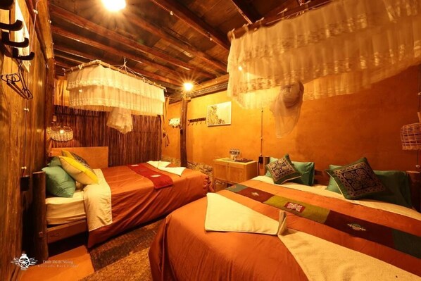 A cozy room with two beds, wooden beams, and hanging curtains.