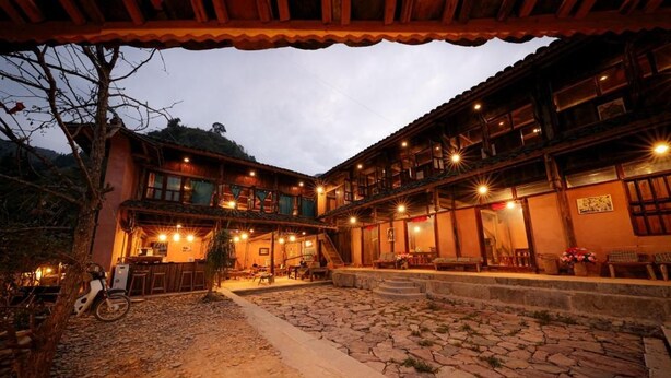 Un patio de piedra tradicional con un edificio de madera que cuenta con varios balcones y una zona de estar cubierta.