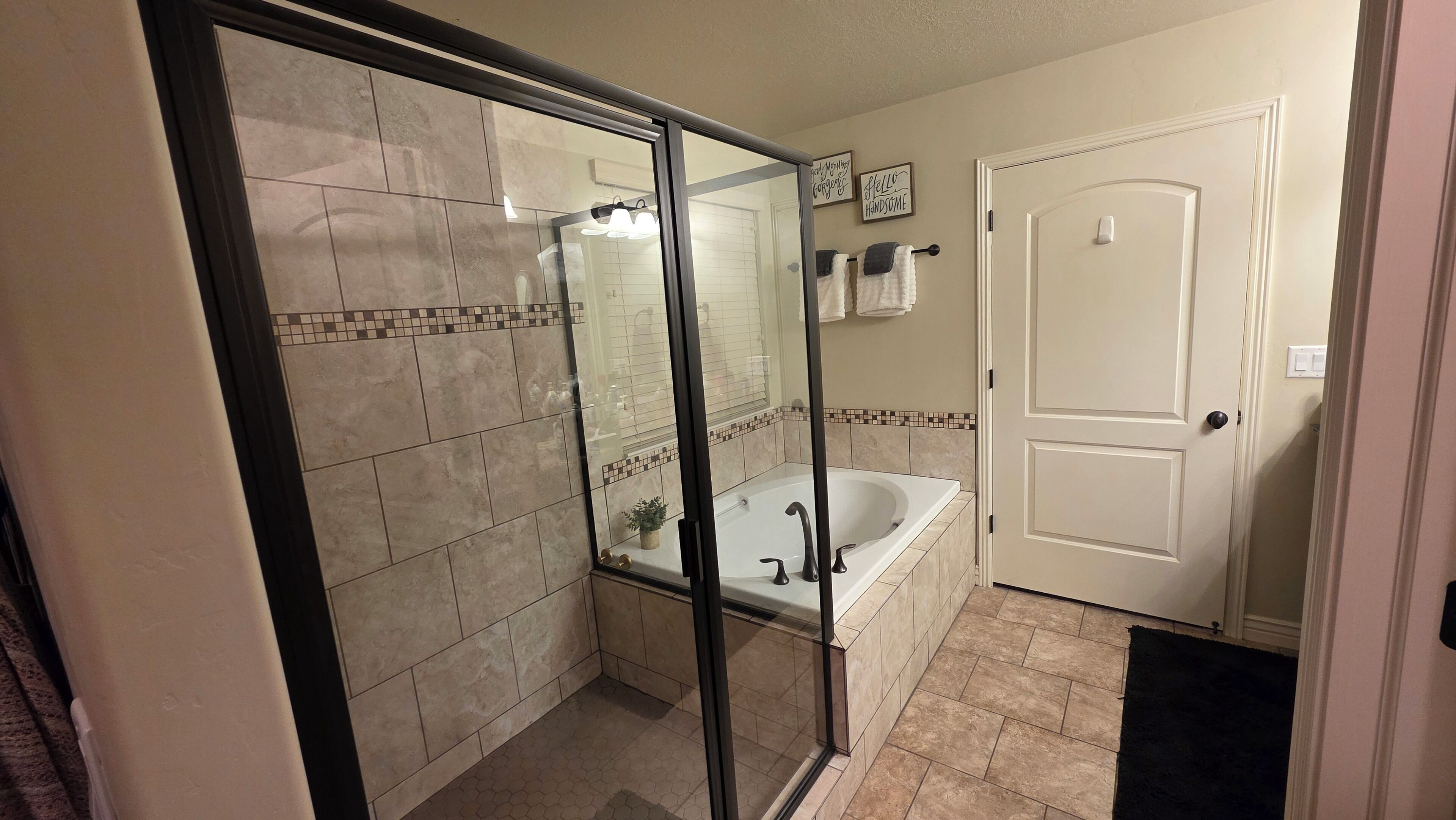 A bathroom with a glass-enclosed shower, a bathtub, and a door.
