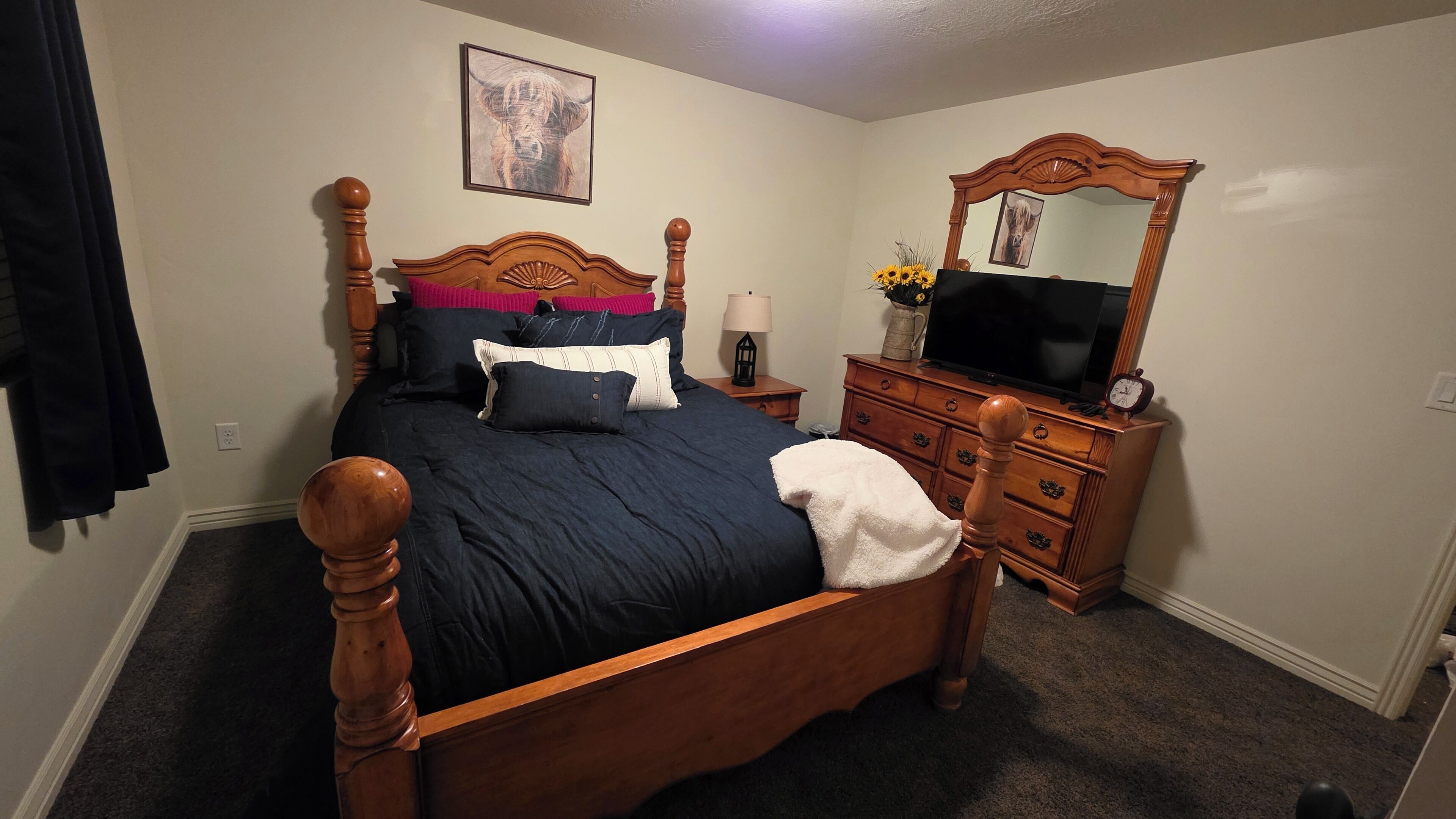 A bedroom with a wooden four-poster bed, a dresser, a television, and a mirror.