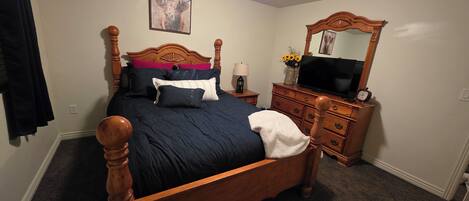 A bedroom with a wooden four-poster bed, a dresser, a television, and a mirror.