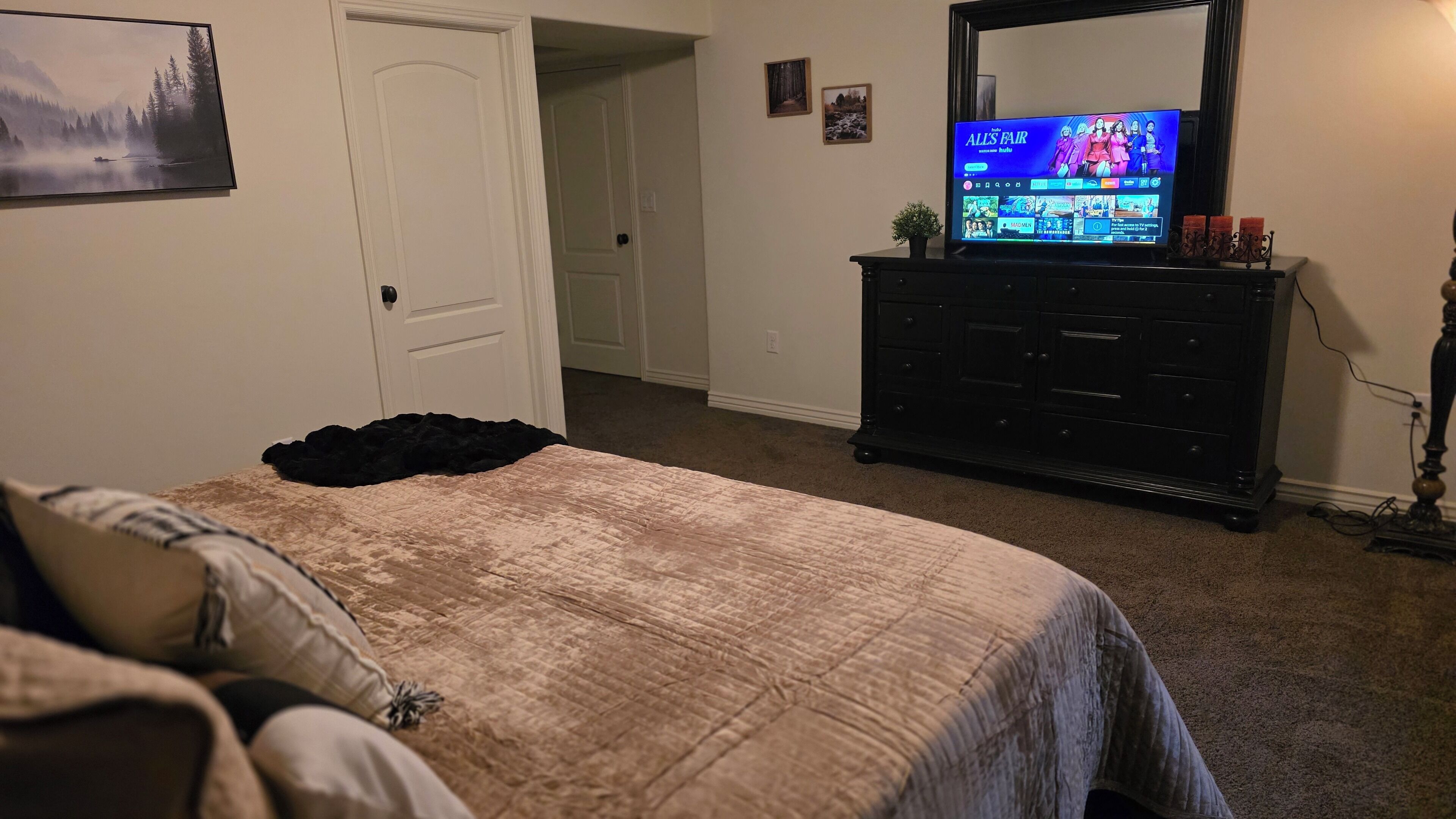 A bedroom with a bed, a dresser, and a television displaying a show.