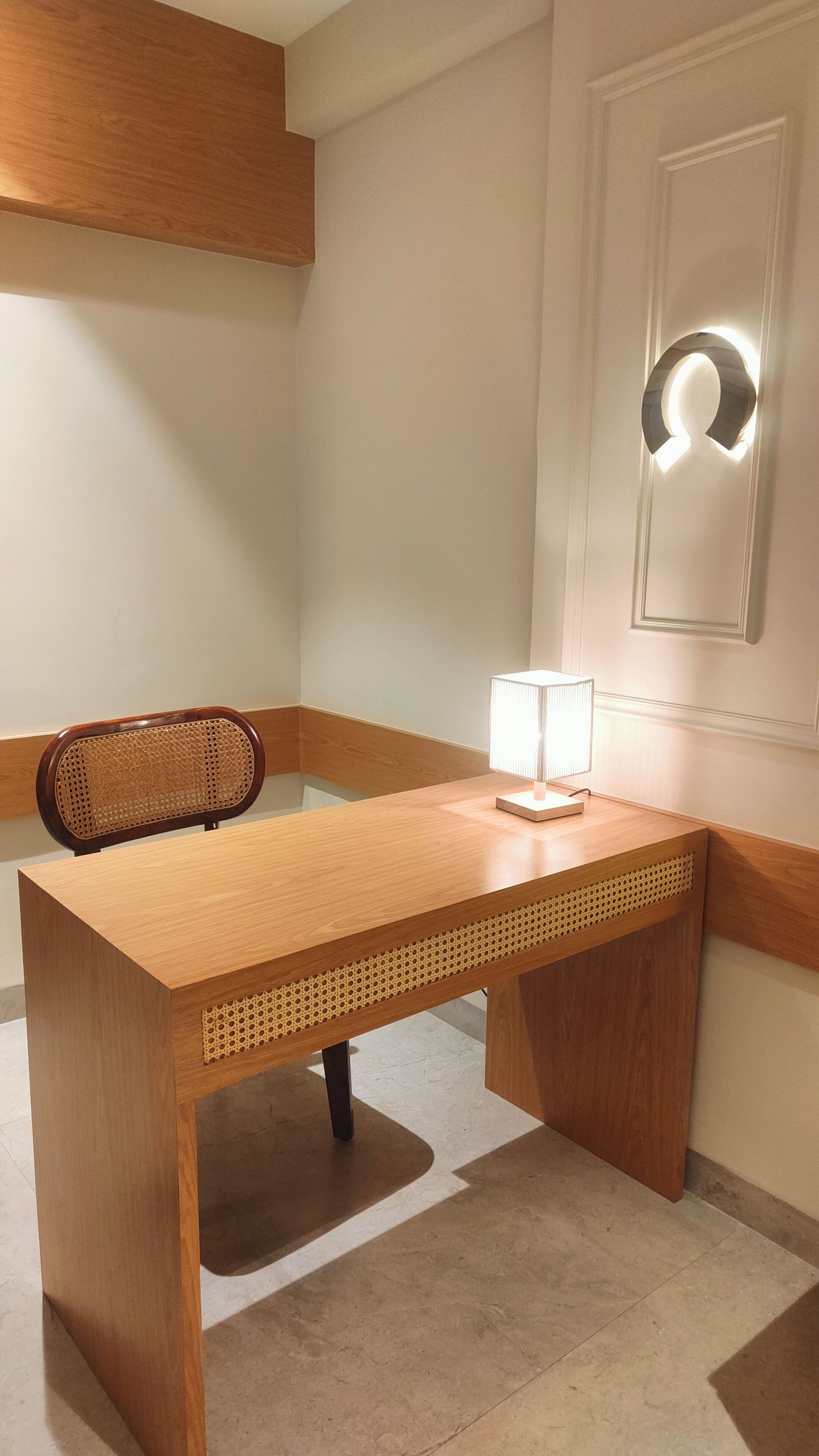 Un bureau d’angle avec un bureau en bois, une chaise, une lampe et un panneau décoratif mural.