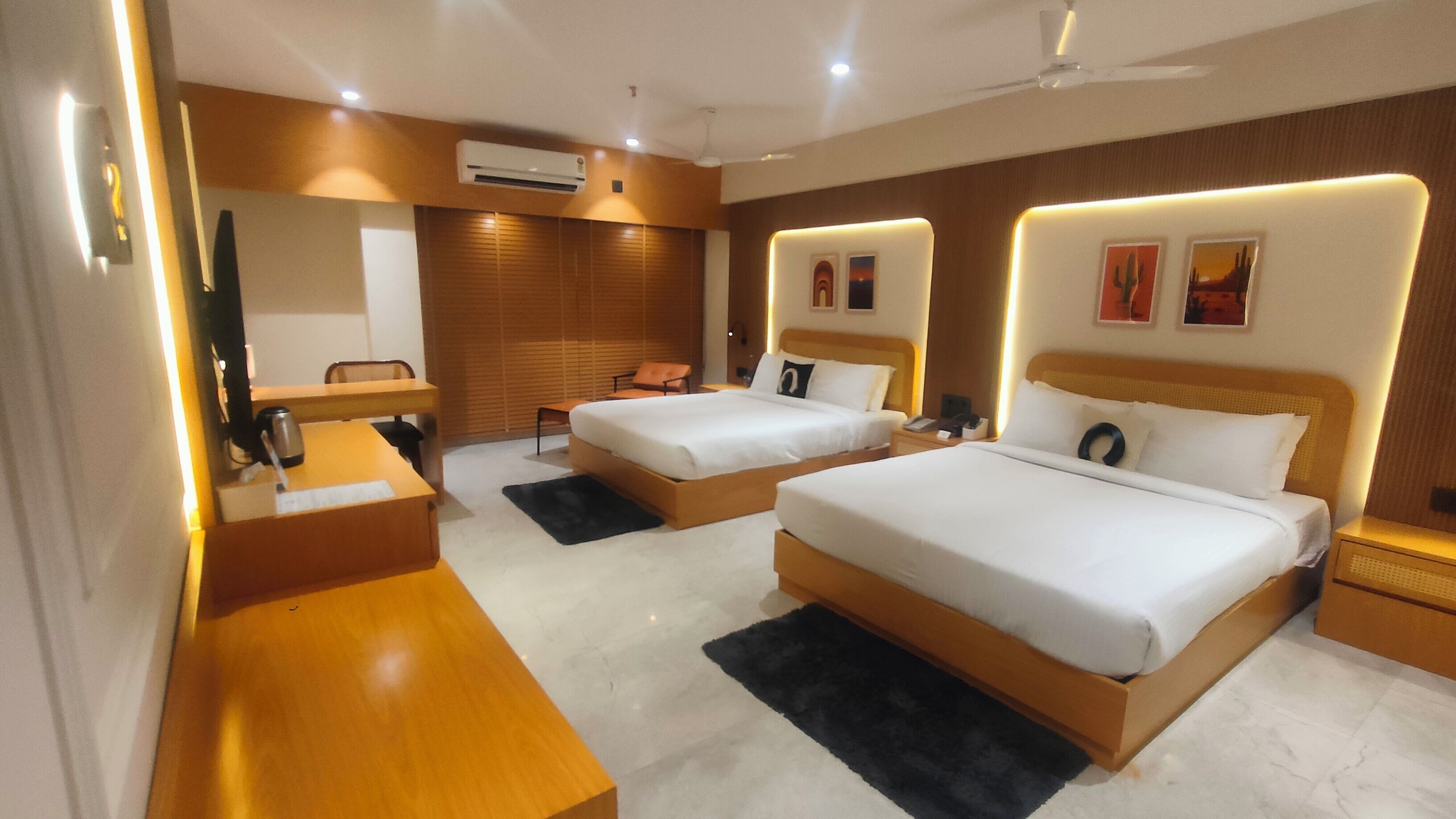 Ein Hotelzimmer mit zwei Betten, einem Schreibtisch, einem Sessel, einer Klimaanlage und einem Deckenventilator.