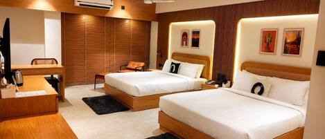 A hotel room with two beds, a desk, a chair, a coffee maker, and artwork on the walls.