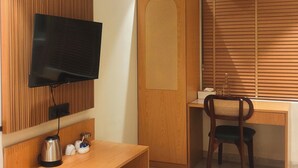 Habitación con una televisión de pantalla plana montada en un panel de madera, un escritorio de madera con una silla, un equipo de aire acondicionado y un armario de madera.