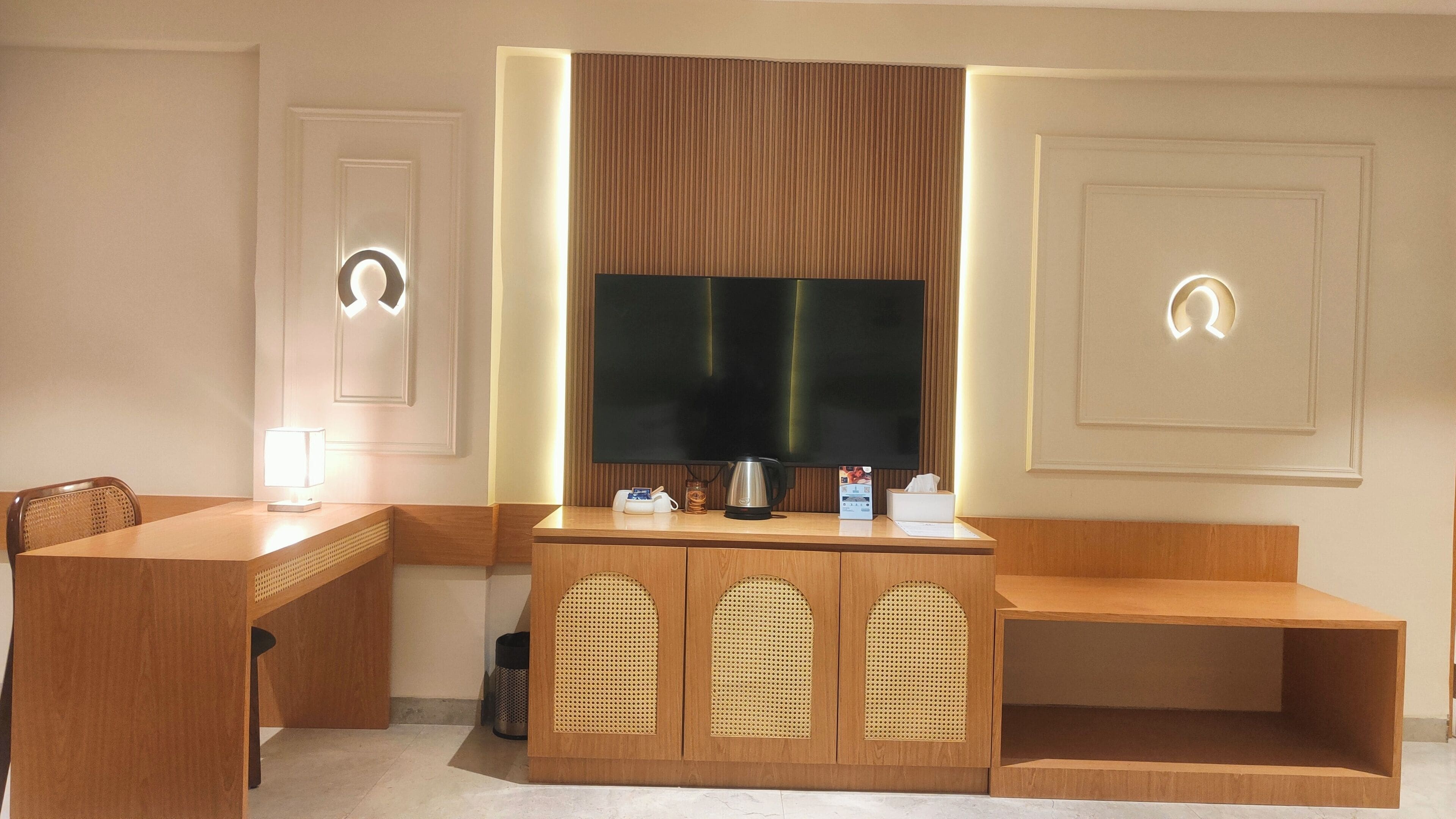 A hotel room with a wooden desk, a television, a coffee maker, and a trash can.