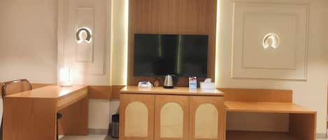 A hotel room with a wooden desk, a television, a coffee maker, and a trash can.