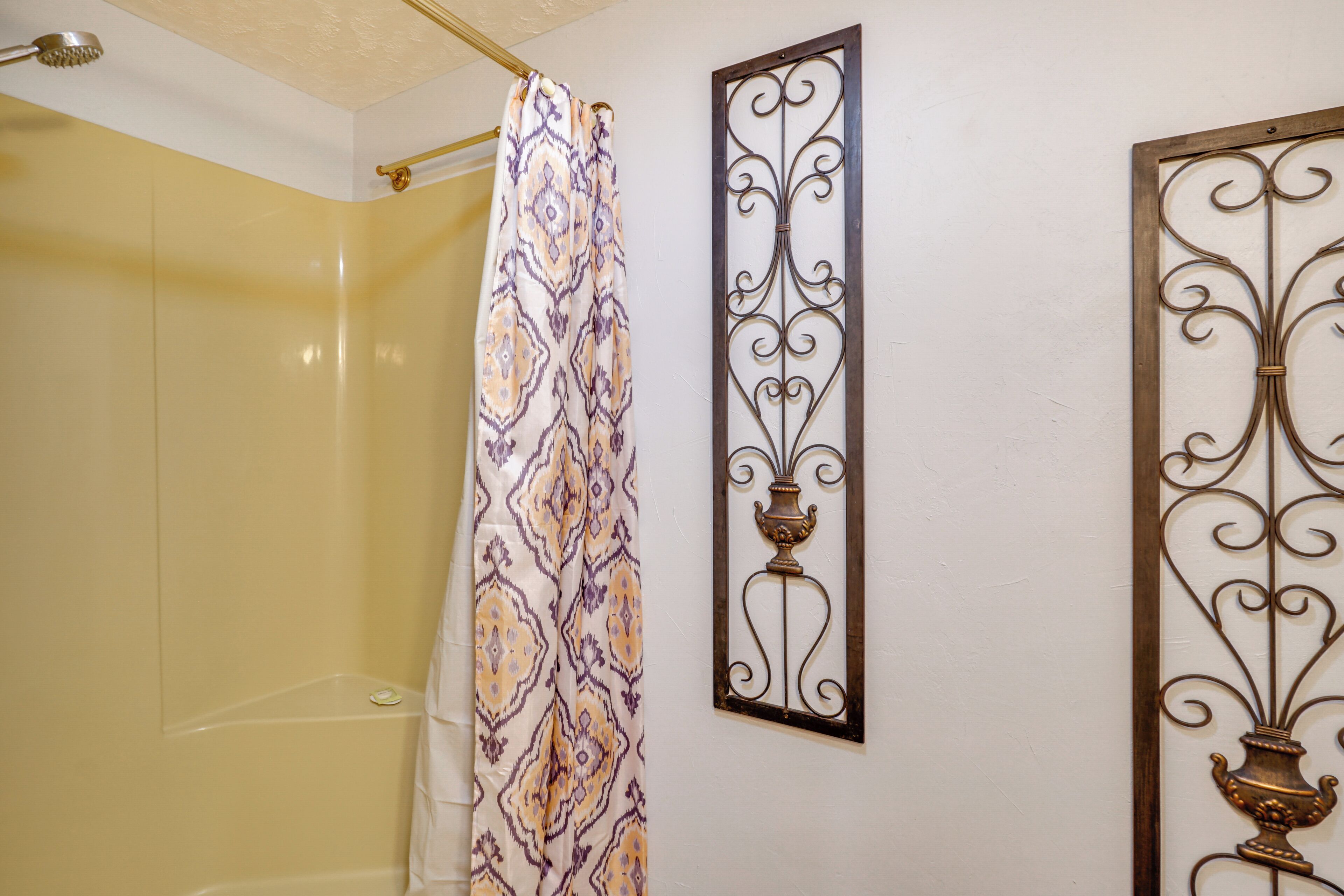 A bathroom with a shower curtain, a decorative wall piece, and a shower head.