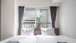 A hotel room with a large bed, two pillows, a window with curtains, and a view of buildings outside. - MOTTO (Sapporo)