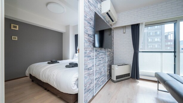 A modern bedroom with a bed, a bench, a TV, and a large window. - MOTTO (Sapporo)