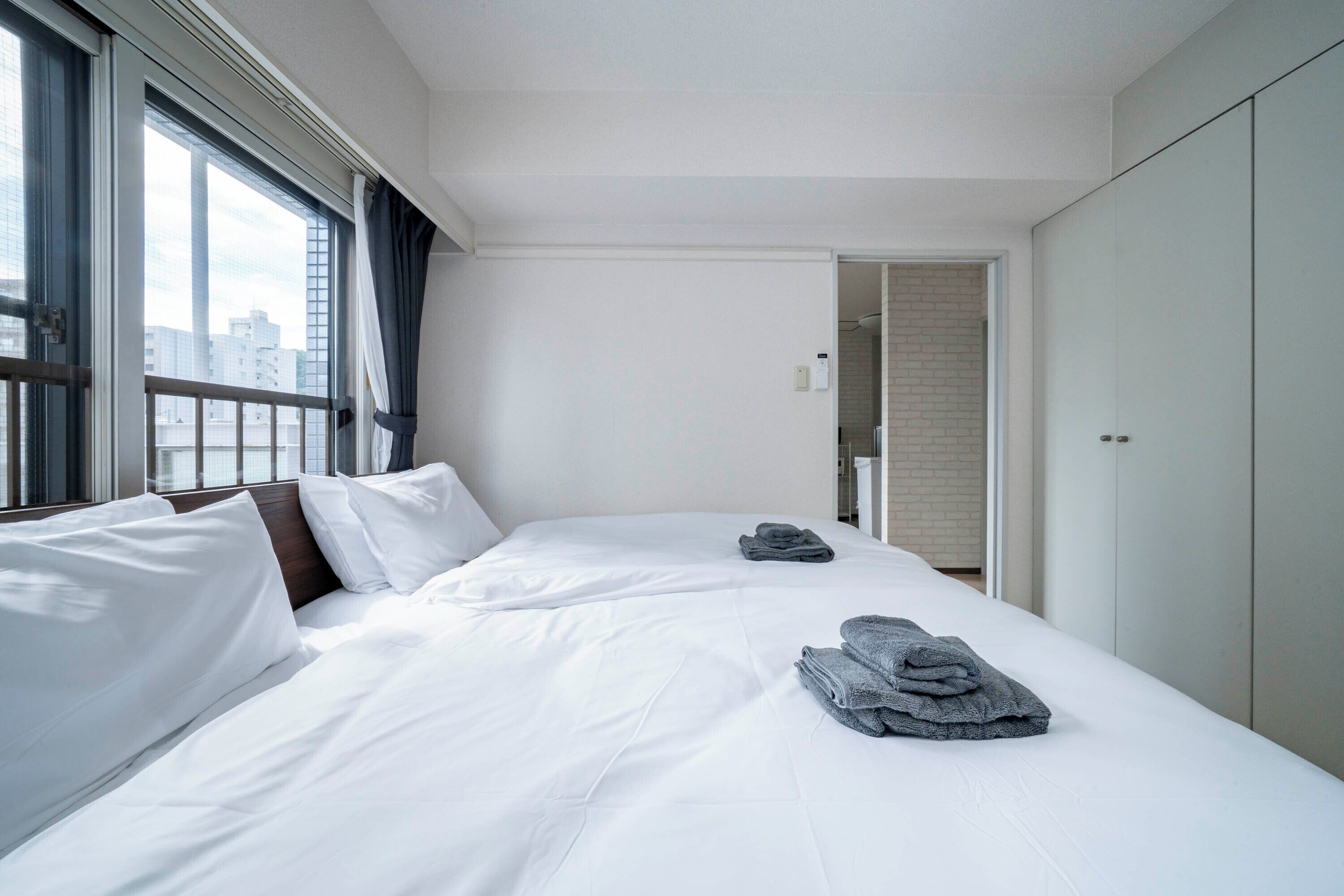 Una habitación de hotel con una cama grande, un armario y un ventanal con cortinas.