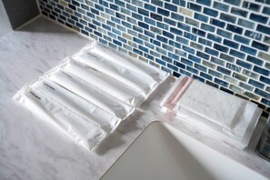 A bathroom with a tiled backsplash, a marble countertop, and neatly arranged toiletries in plastic bags. - MOTTO (Sapporo)
