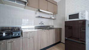 A modern kitchen with stainless steel appliances, wooden cabinets, and a white tiled backsplash. - MOTTO (Sapporo)