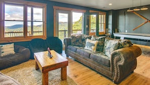 A living room with a leather couch, wooden coffee table, and large windows offering a view of hills. - Ski & Hike: Mars Hill Mountaintop Cabin w/ Views (Mars Hill)