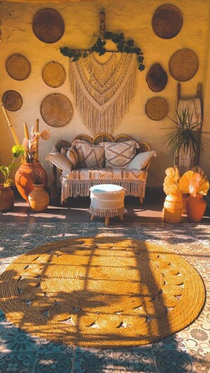 A cozy room with a woven rug, a sofa with patterned cushions, and a wall decorated with circular woven items. - Casa Rossa Resort (Pune)