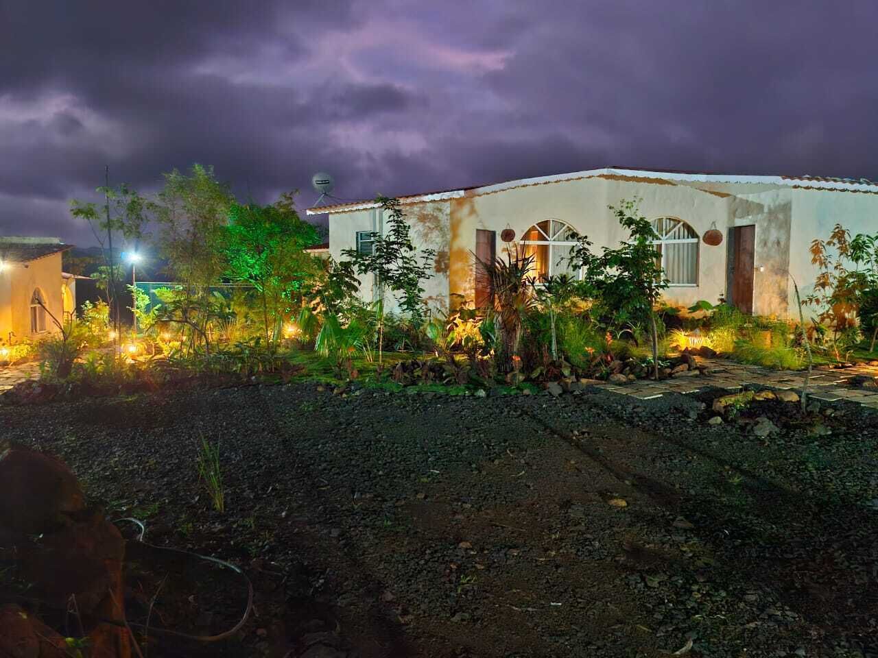A rustic building with a white facade, surrounded by lush greenery and a well-maintained garden.