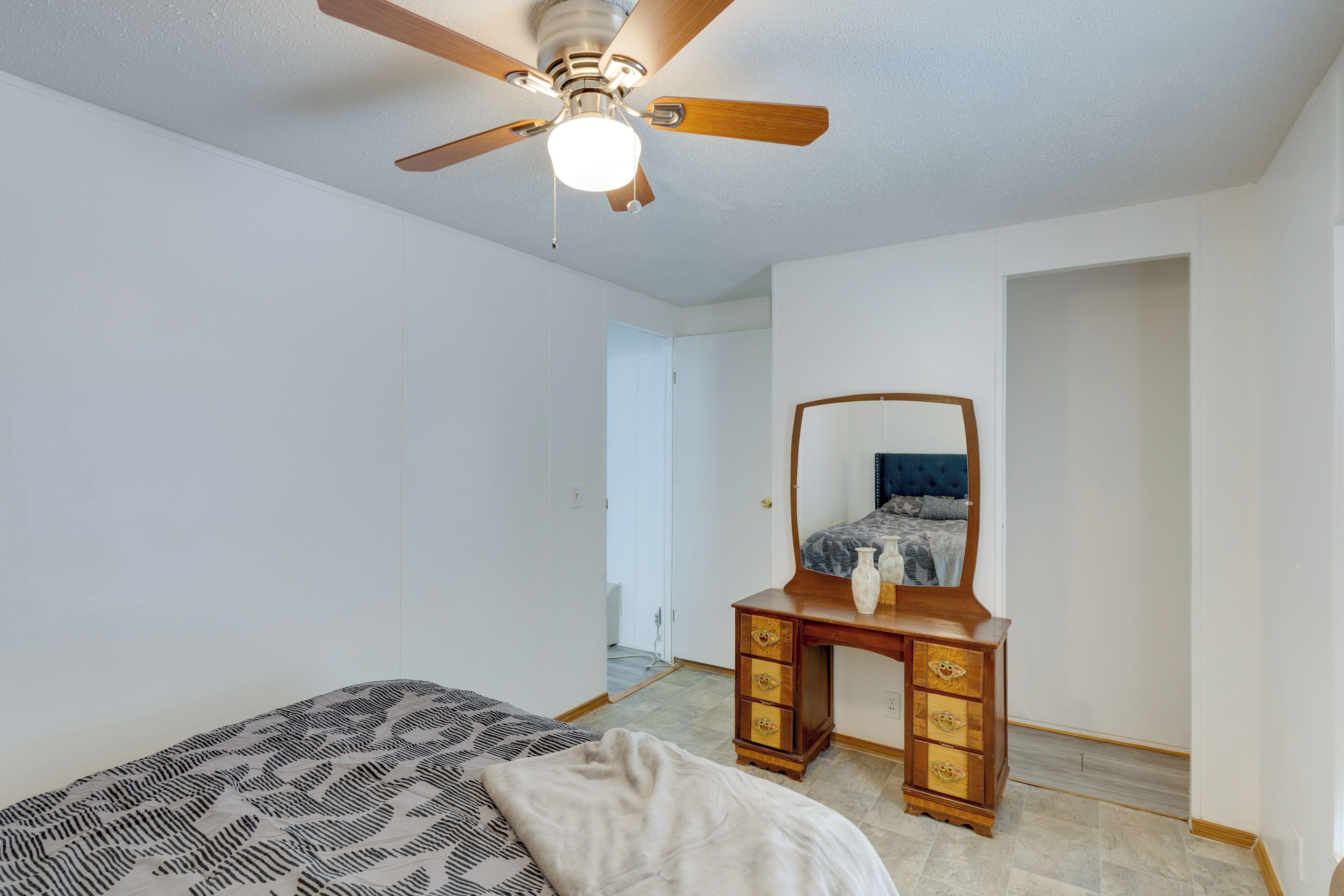 A bedroom with a bed, a dresser, a ceiling fan, and a door leading to another room.