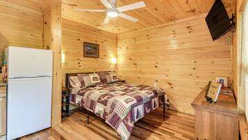 A cozy cabin room with a bed, a white refrigerator, a ceiling fan, and a mounted television.