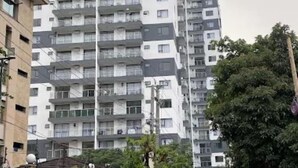 Un edificio residencial alto con varios balcones, entrada protegida y vegetación circundante.