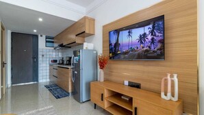 Una cocina moderna con microondas integrado, refrigerador y armarios de madera. Un televisor de pantalla plana está montado en la pared sobre un mueble bajo de madera.