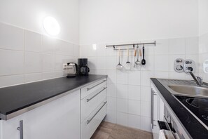 Une cuisine avec des meubles blancs, un plan de travail noir, une machine à café et des ustensiles de cuisine suspendus.
