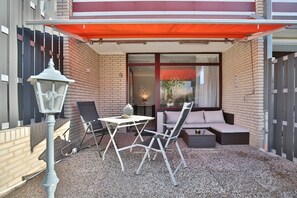 A covered patio with a table and chairs, a lamp, and a seating area with cushions.
