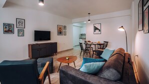 Ein modernes Wohnzimmer mit einer Couch, Sesseln, einem Couchtisch und einem Fernseher. Es gibt einen Essbereich mit einem Tisch und Stühlen.