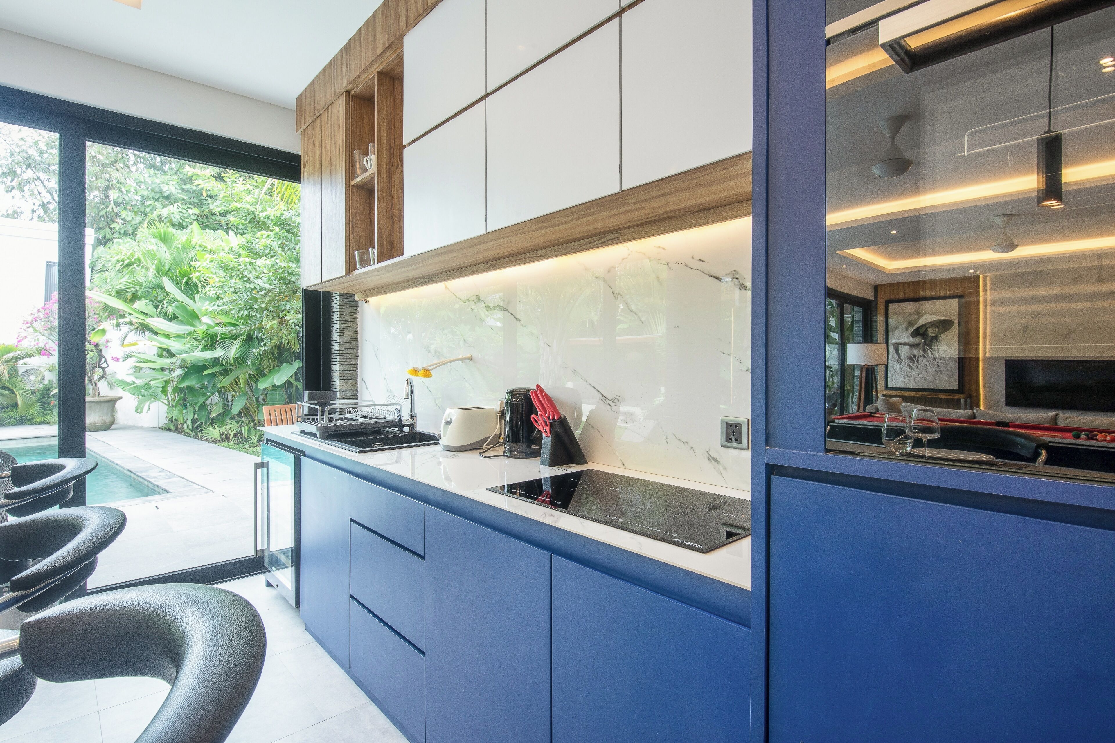 A modern kitchen with a marble countertop, built-in cabinets, and a glass door leading to a pool area.