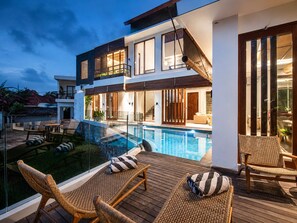 A modern two-story house with a swimming pool, outdoor seating, and a balcony.