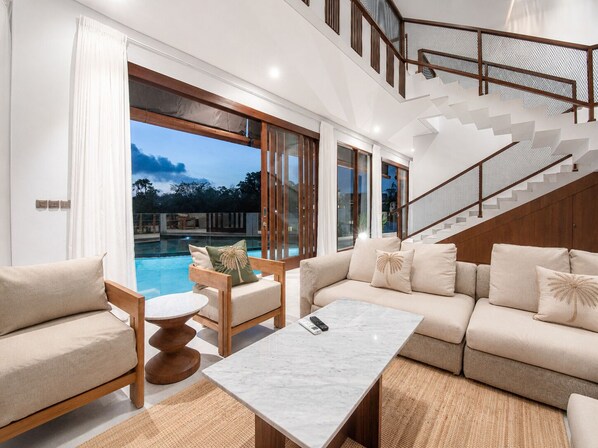 A modern living room with a pool view, a staircase, and a poolside seating area. - 5BR Canggu Retreat Steps to Beach, Ricefield View (Canggu)