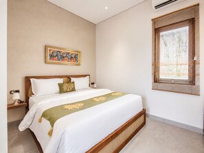 A hotel room with a bed, a wall-mounted painting, a window with blinds, and a bedside table with a lamp.