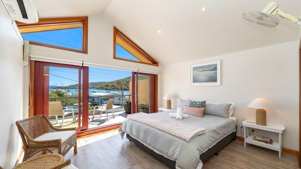 Une chambre à coucher avec un lit, des tables de chevet, une chaise et une vue sur la mer et les bateaux.