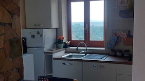 Een keuken met een stenen boog, een raam met uitzicht, een laptop op het aanrecht en gele stoelen.