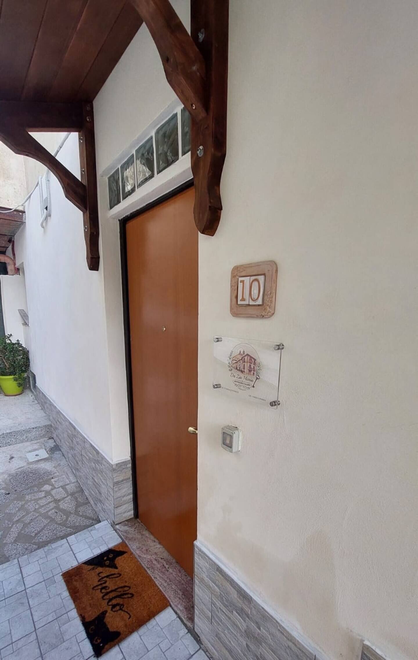 A hallway with a wooden door, a doormat, a number plaque, and a small framed picture on the wall.