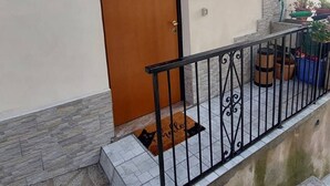 Een gevelingang met een houten deur, een klein balkon met een metalen hekwerk en een bloempot aan de rechterkant.