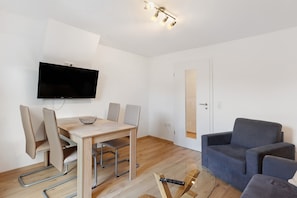 A modern living room with a flat-screen TV, a dining table with chairs, a sofa, and a glass coffee table.