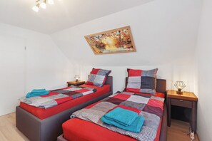 A bedroom with two beds, a nightstand with a lamp, a painting on the wall, and a wooden floor.