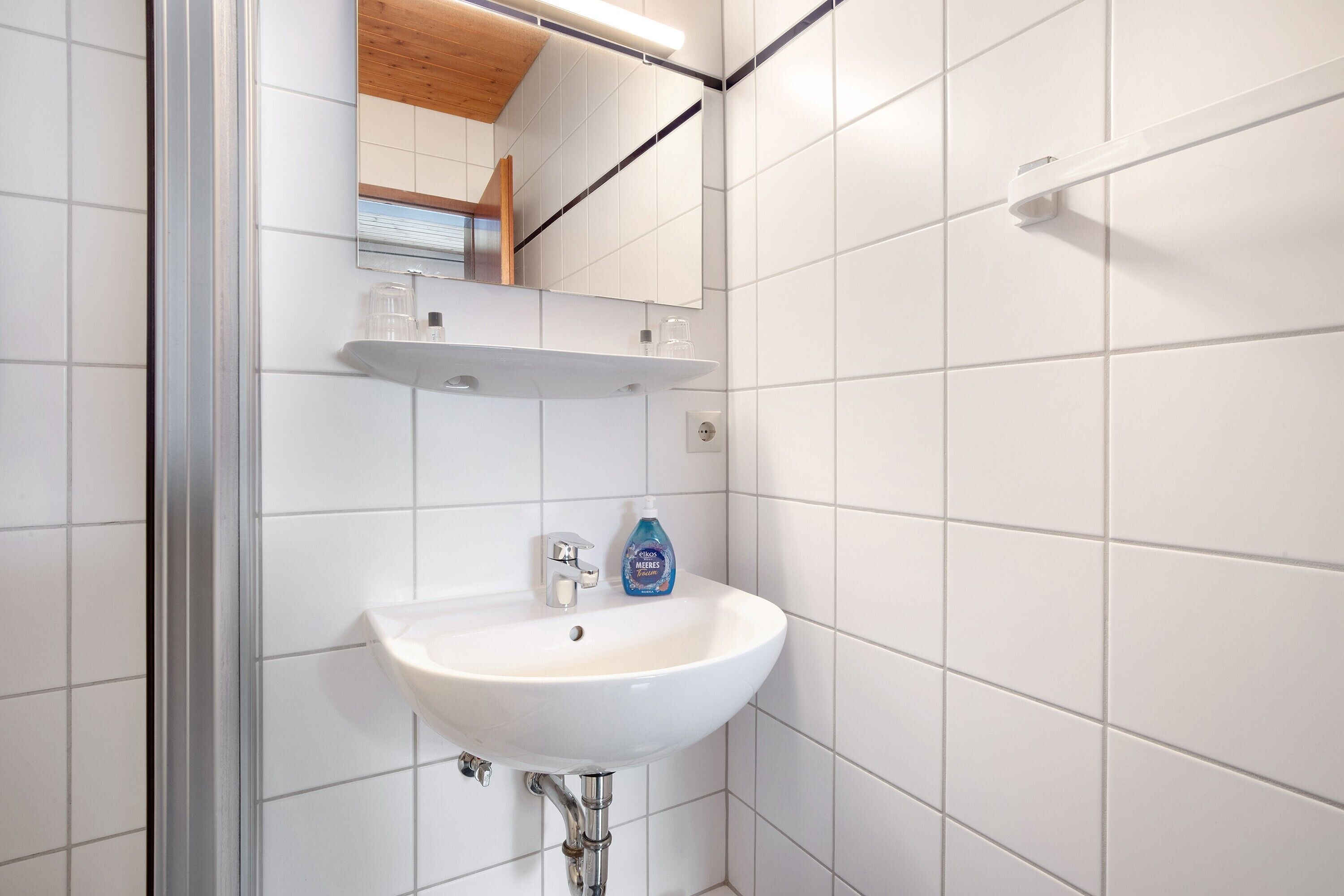 A bathroom with a white sink, a mirror, and a shelf with toiletries.