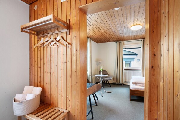 A wooden interior with a bed, a chair, a table, and a hanging rack.