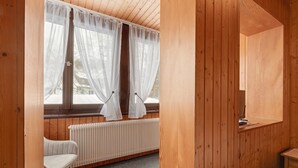 A wooden-paneled room with a radiator, a chair, and a window with sheer curtains. - Apartment 'Zimmer 32' (Nürtingen)