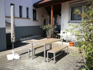 An outdoor patio with a wooden table and benches, surrounded by potted plants and a white wall. - Apartment 'Zimmer 32' (Nürtingen)