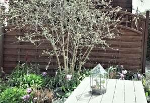 A garden with a wooden fence, a table with a glass lantern, and purple flowers. - Apartment 'Zimmer 32' (Nürtingen)