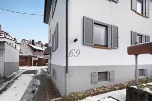 A residential building with a number '69' on the side, a window with shutters, and a small outdoor area with rocks and snow. - Apartment 'Zimmer 32' (Nürtingen)