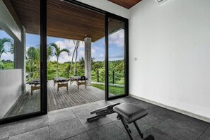 A modern room with a large sliding glass door leading to an outdoor deck with massage tables and a view of a lush landscape. - Villa Maxime by BaliSuperHost (Bali)