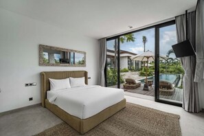 A bedroom with a large bed, a television, and a view of an outdoor pool area. - Villa Maxime by BaliSuperHost (Bali)